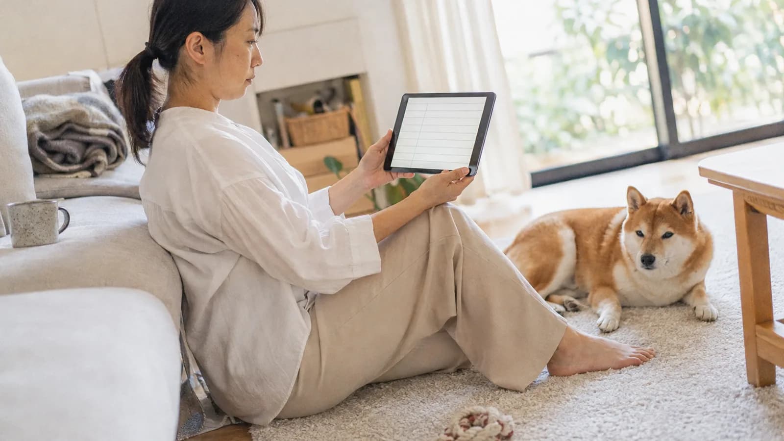 床に座ってタブレットの記録の画面を見る女性と、すぐ横で伏せる赤い柴犬