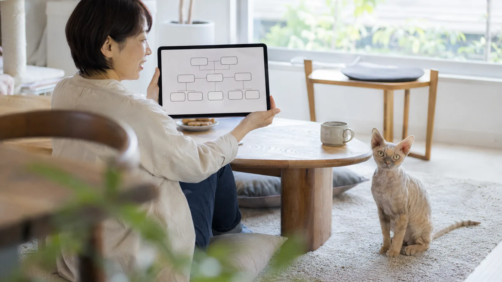 床でタブレットの家系図の画面を見せる女性と、そばのラグに座るデボンレックス