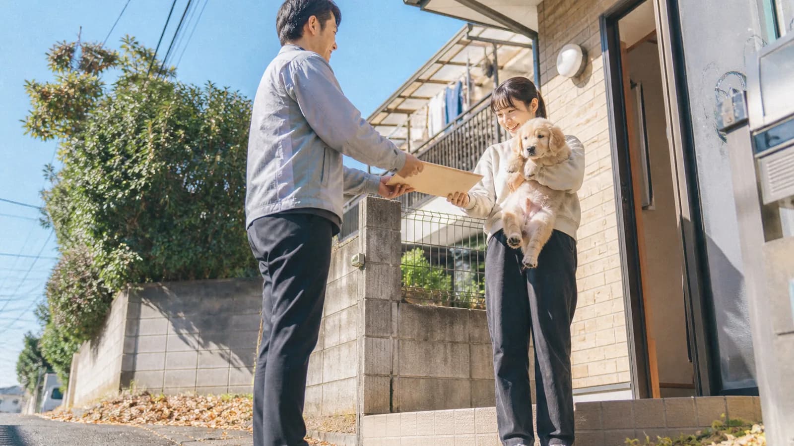 玄関先で、子犬を抱いた女性に書類の入った大きな封筒を手渡す男性