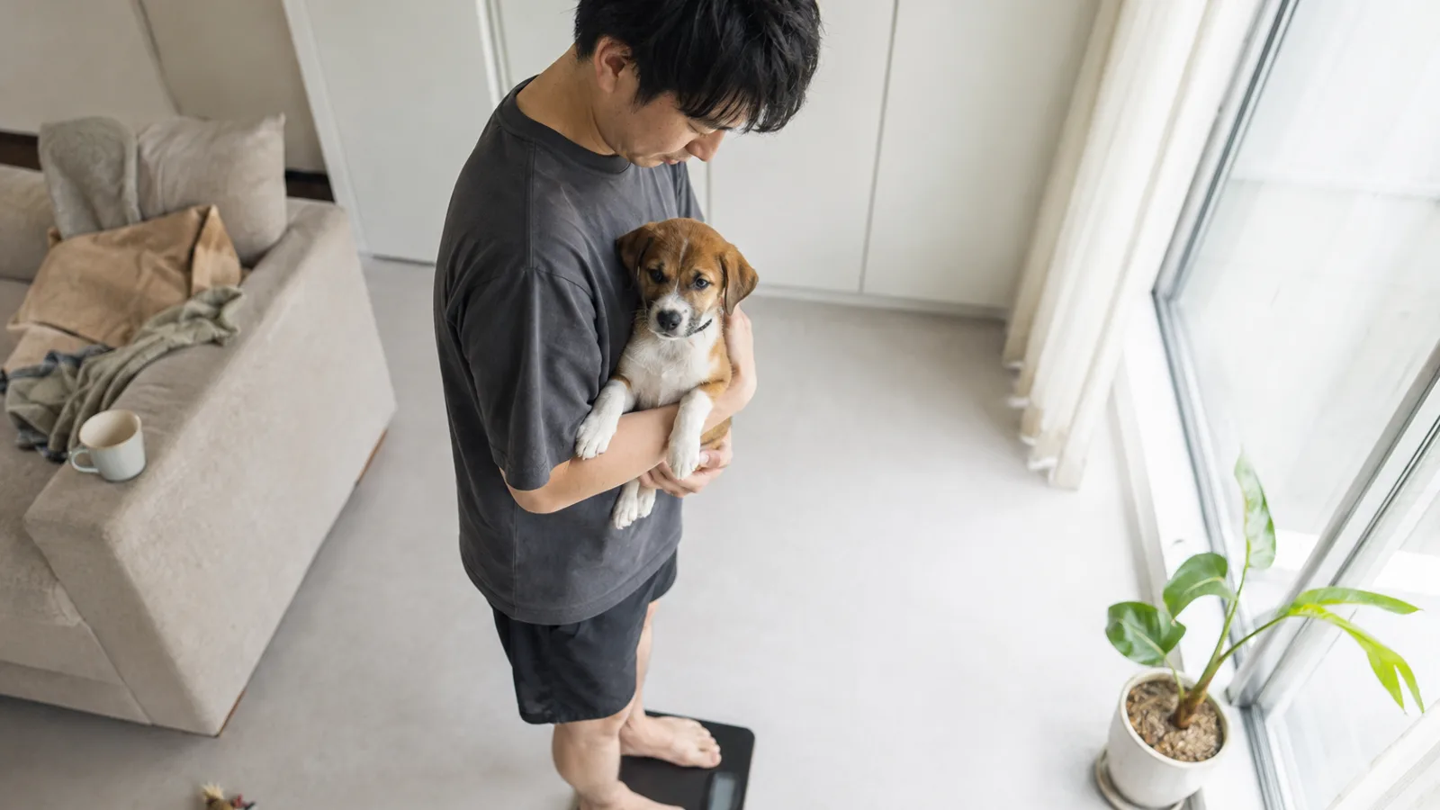 子犬を胸に抱いたまま体重計の上に立つ男性