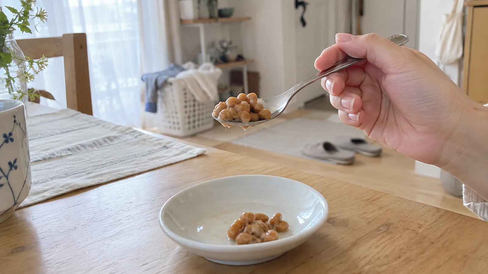 小さな白い皿の上で、ひとさじの納豆を小さじにのせた手元