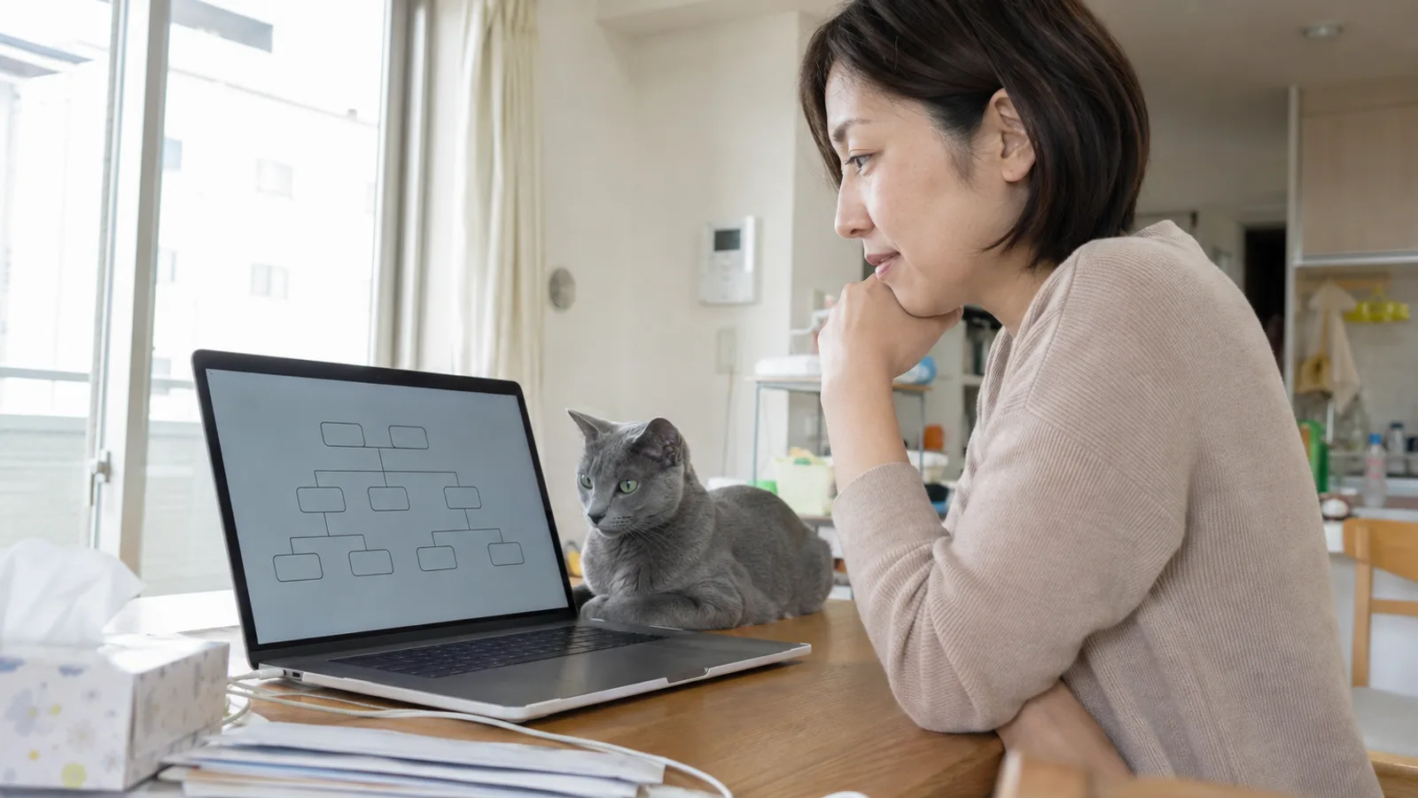 ダイニングでノートパソコンの家系図の画面を見る女性と、テーブルの上に伏せて同じ画面のほうを見るロシアンブルー