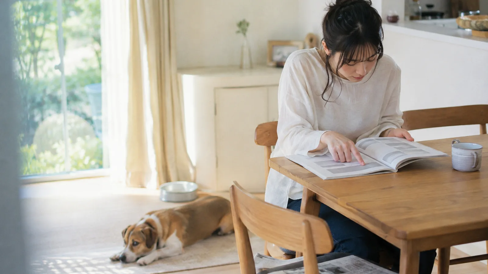 架空の冊子の見出しの帯を指先でなぞる女性と、足元に伏せる中型ミックス犬